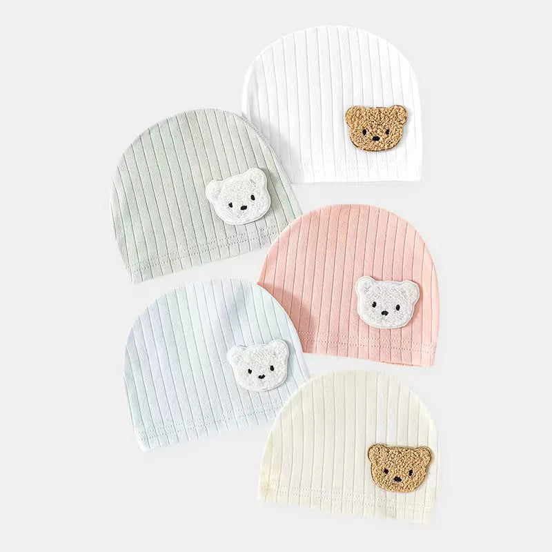 A collection of baby beanie caps with cute ears in various colors, each featuring a bear face detail.