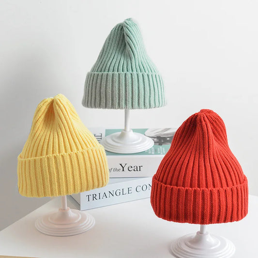 Three ribbed knitted beanies in yellow, green, and red colors displayed on mannequin heads against a light background.